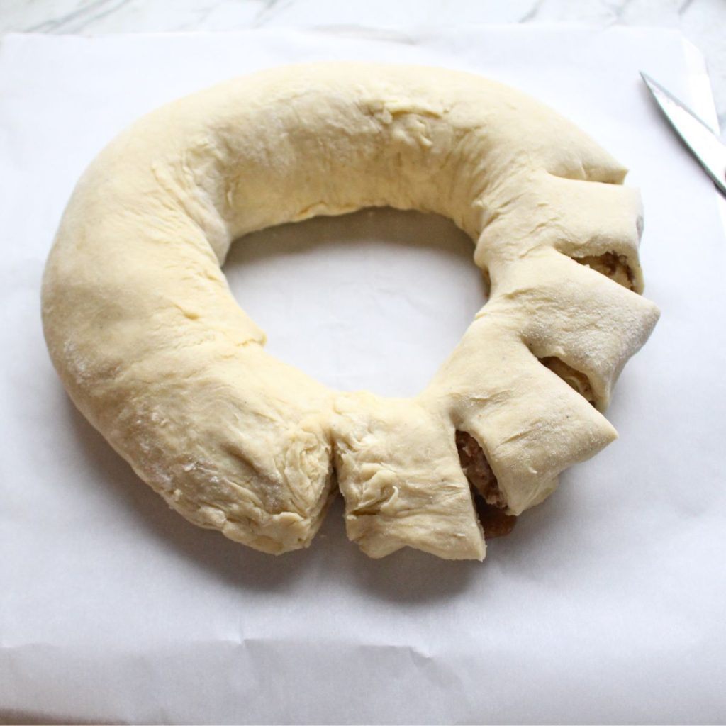 Swedish cardamom coffee cake in the process of cutting the pieces around the ring 1-2 inches apart.