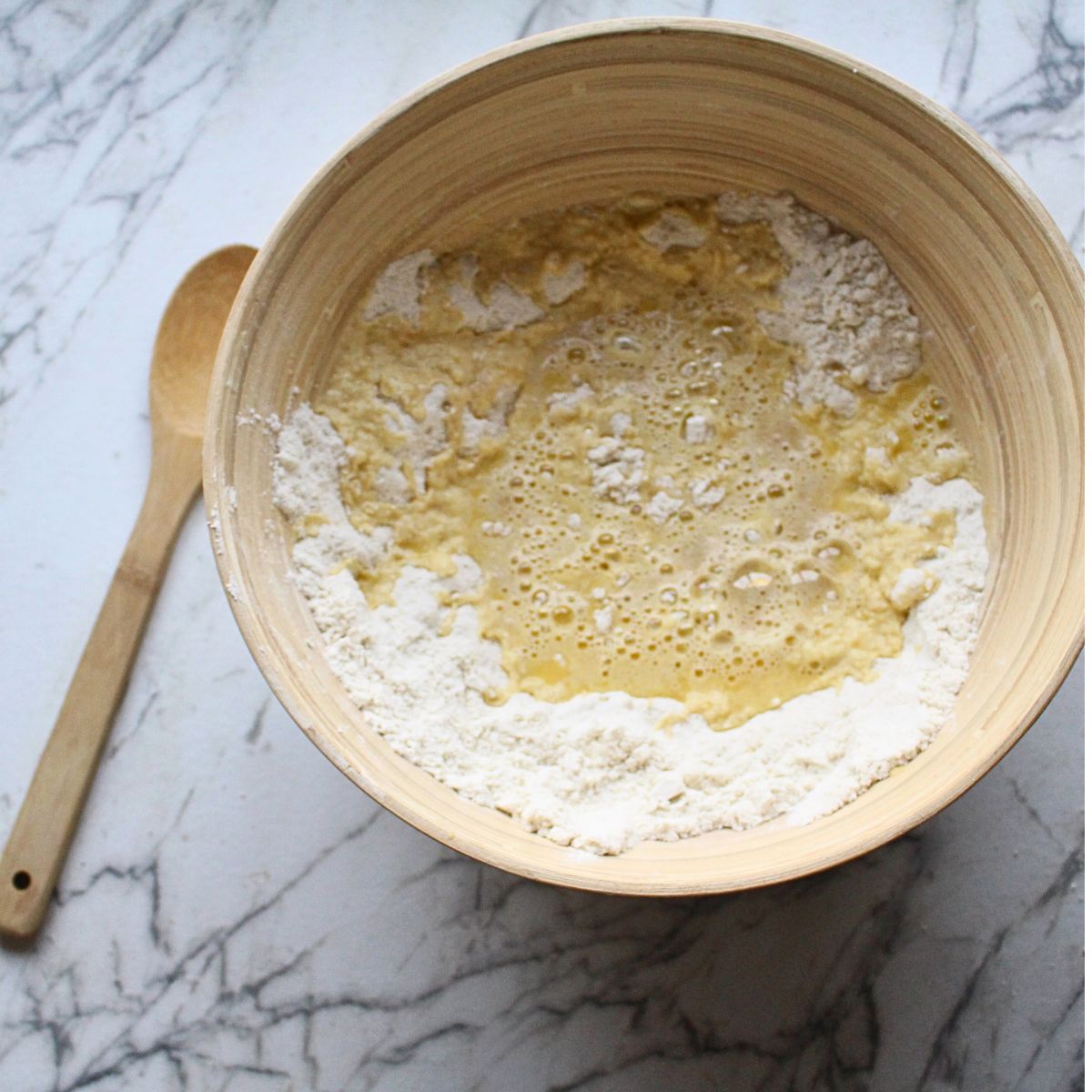 A wooden bowl with dry ingredients and wet ingredients (liquid) in the center to make Swedish cardamom coffee cake.