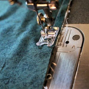 The contrasting band, trim and pillowcase body being sewn together on the presser foot edge of the sewing machine.