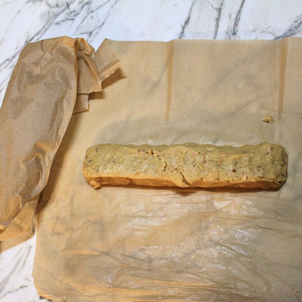 A log of Almond Icebox cookie dough on a piece of parchment paper.