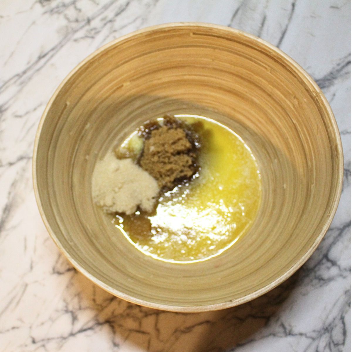 A wooden bowl with melted butter, white sugar and brown sugar in it.