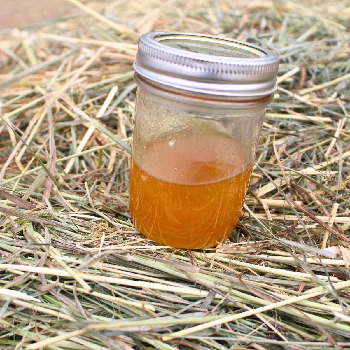 A small jar of honey on a hale bale.