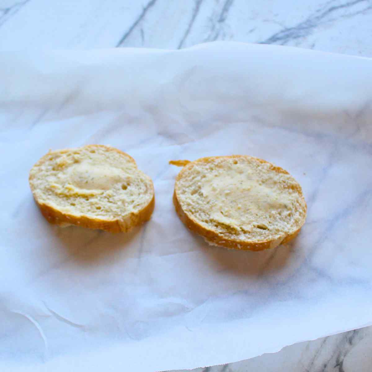 Two slices of french bread spread with garlic butter for homemade garlic bread.