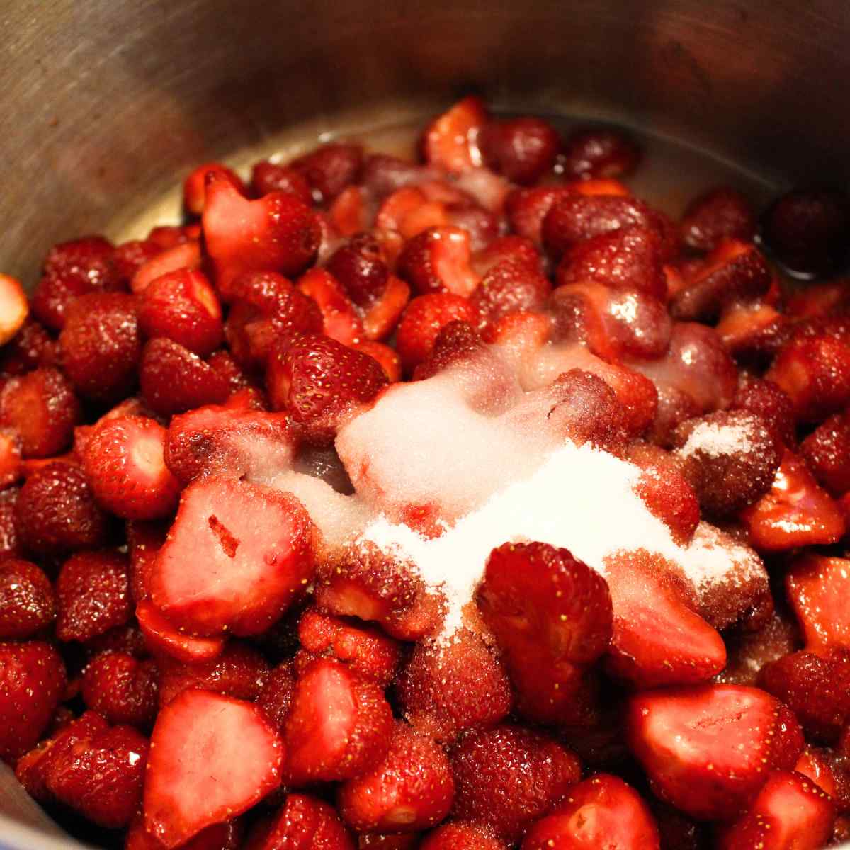 Hulled and cut up strawberries in a pot with sugar and lemon juice for making strawberry sauce.