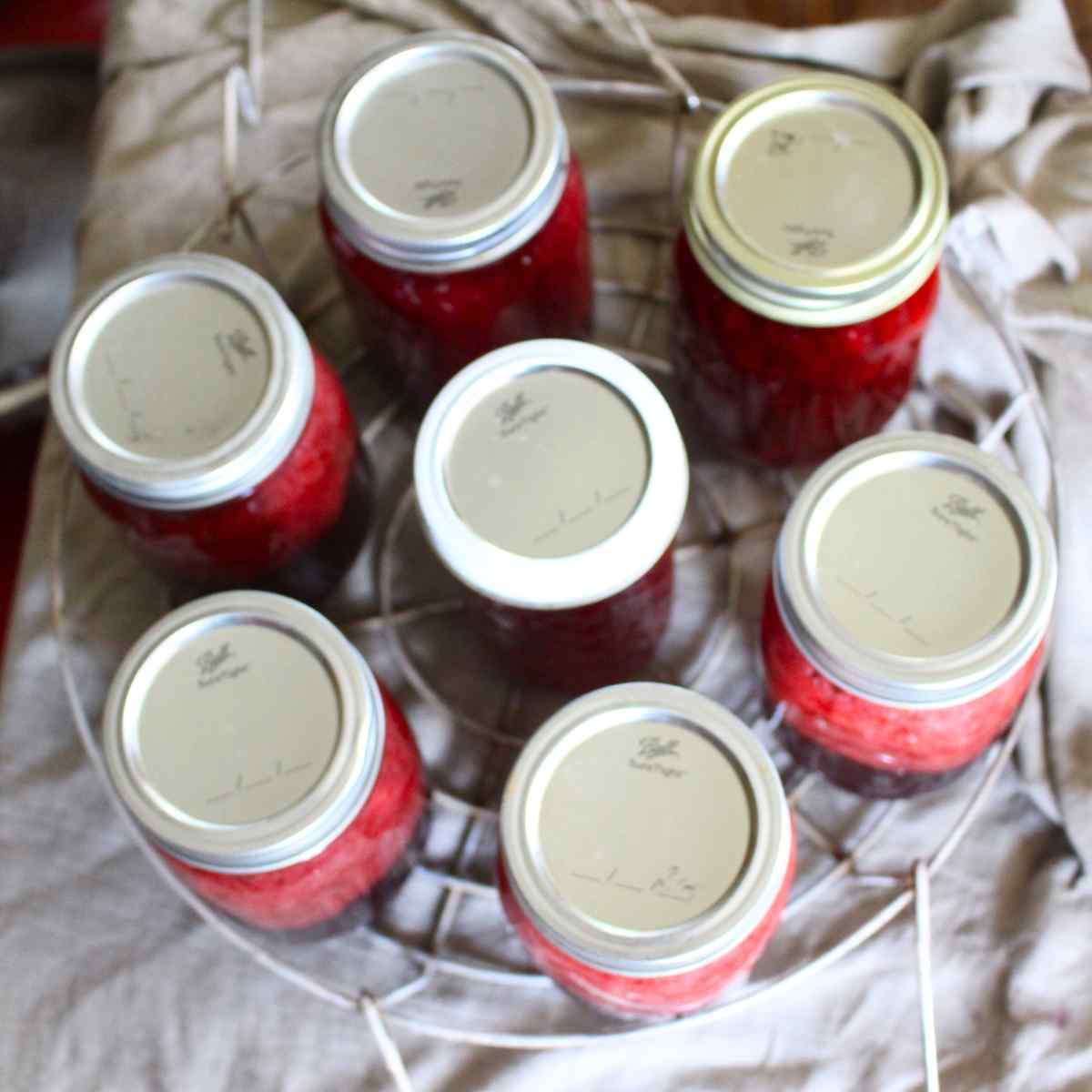 A canner rack filled with jars of strawberry sauce to be water bath canned.