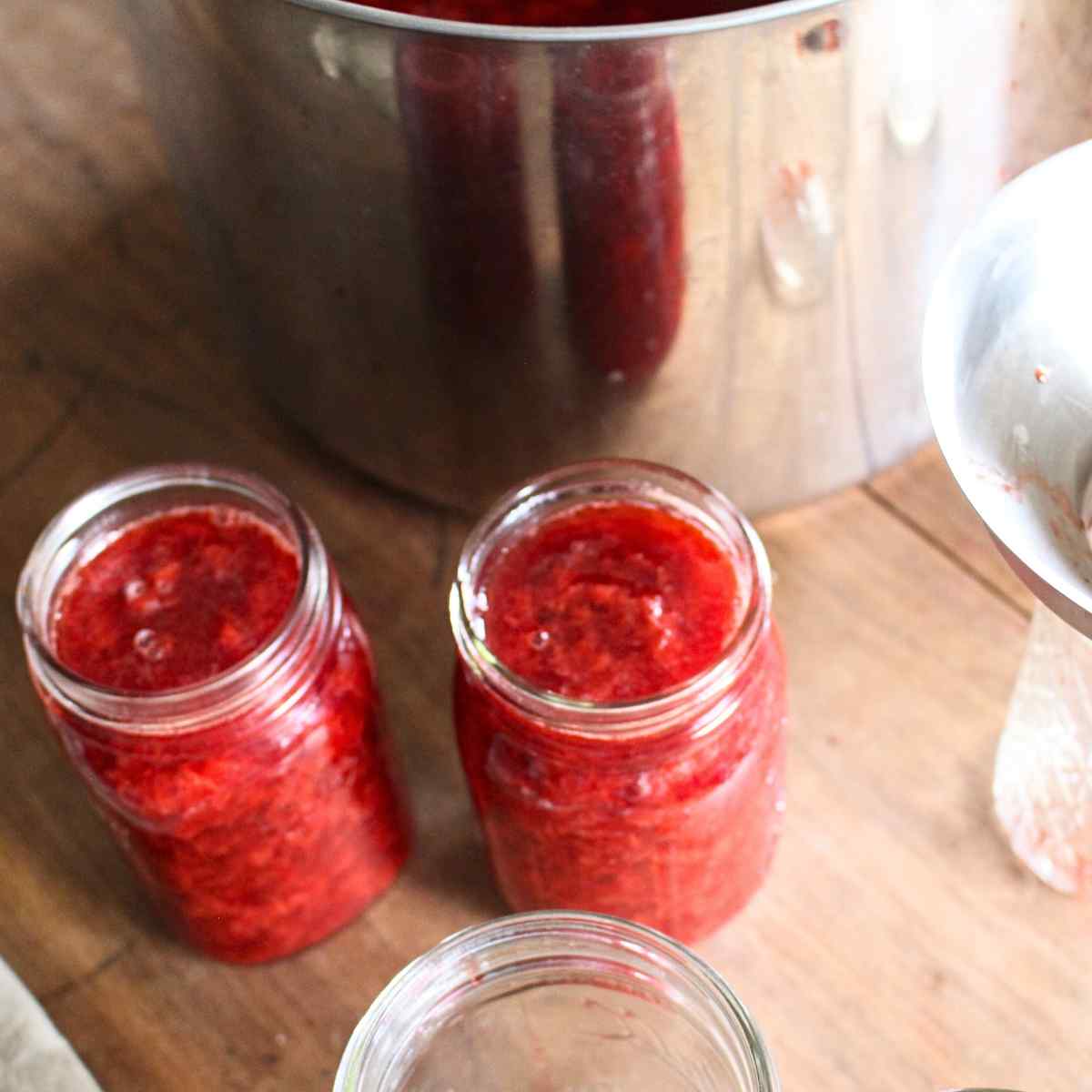 Two pint jars filled with strawberry sauce before the lids and rings have been put on.