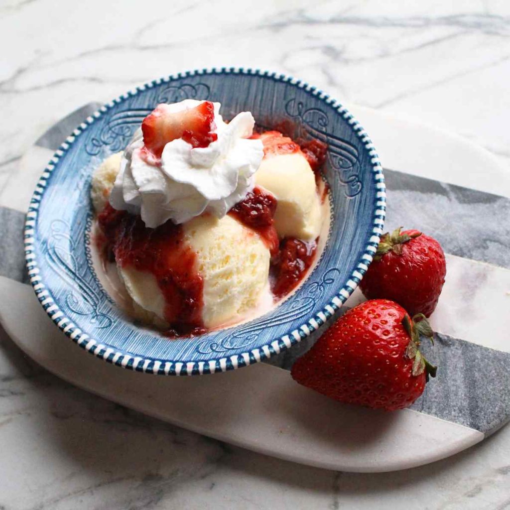 A bowl of ice cream with strawberry sauce on it, and topped with whipped cream and a strawberry.