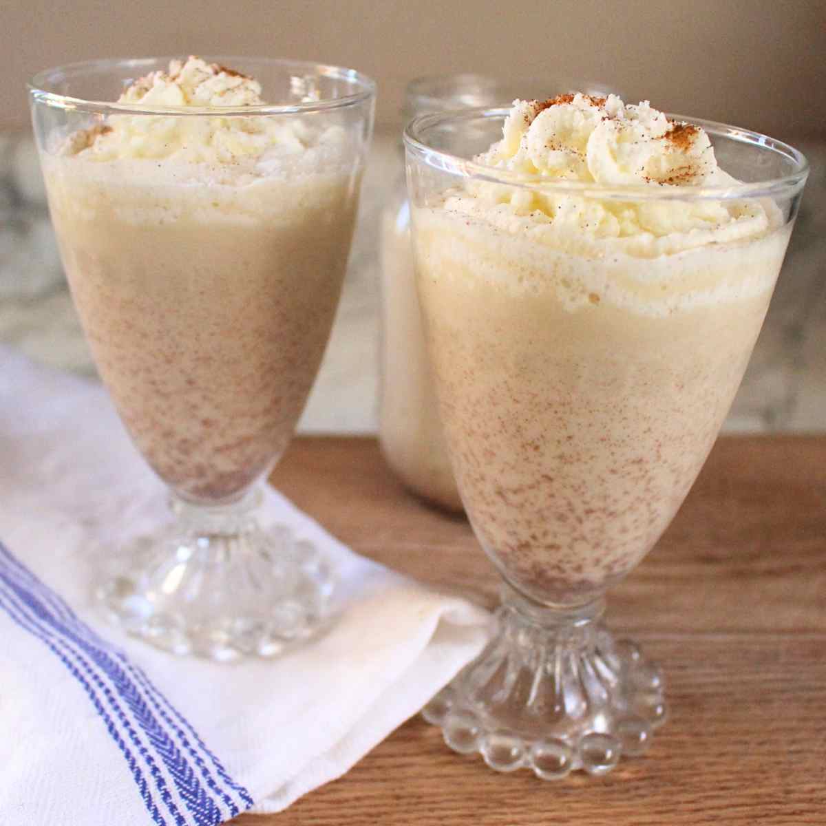 Two glasses of homemade egg nog with whipped cream on top.