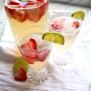 A mason jar with two glasses full of homemade strawberry limeade.