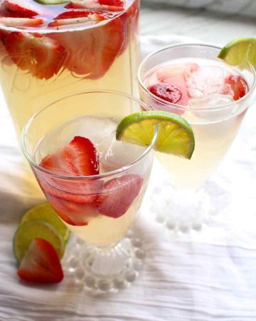 A mason jar with two glasses full of homemade strawberry limeade.