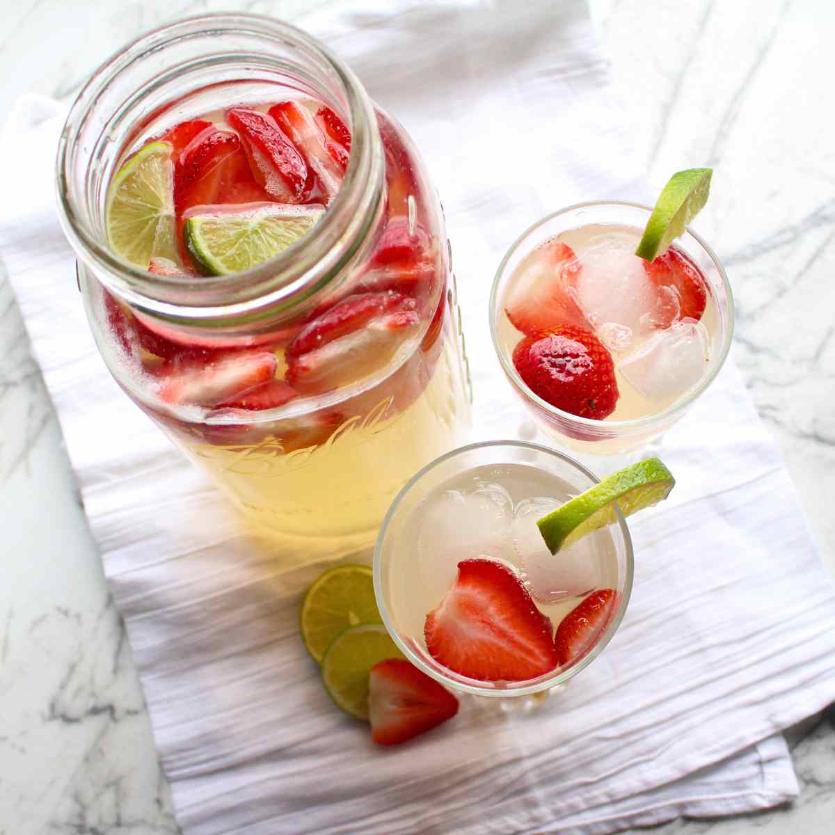 A top view of a mason jar with two glasses full of homemade strawberry limeade.