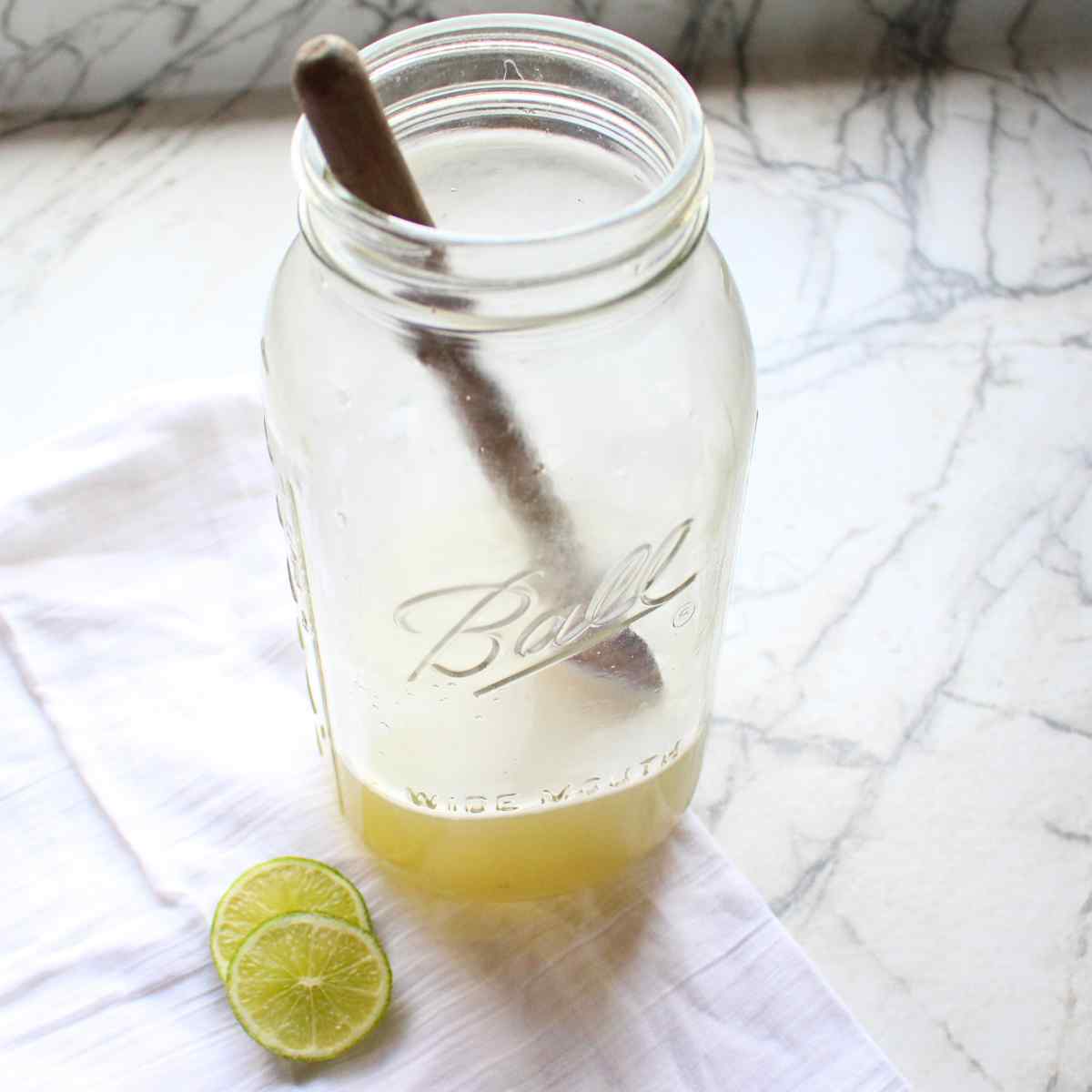 A mason jar with a wooden spoon in it, with homemade limeade concentrate for strawberry limeade.