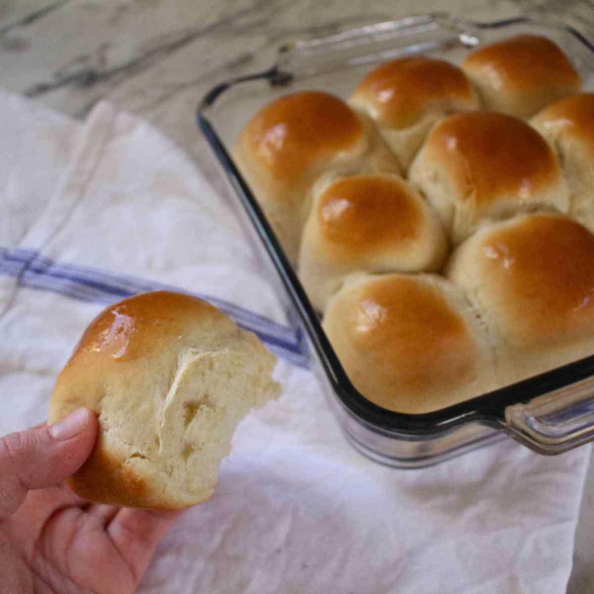 A close up of a lightly, fluffy 1 hour dinner roll with the pan of dinner rolls in the background.