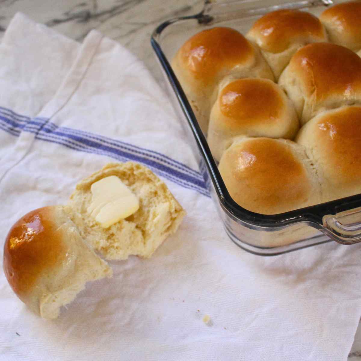 A dinner roll split in half with butter on it, and the pan of dinner rolls next to it.