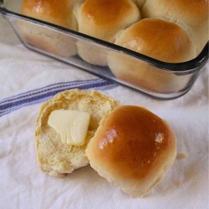 A close up of a buttered 1 hour dinner roll with the pan of dinner rolls in the background.