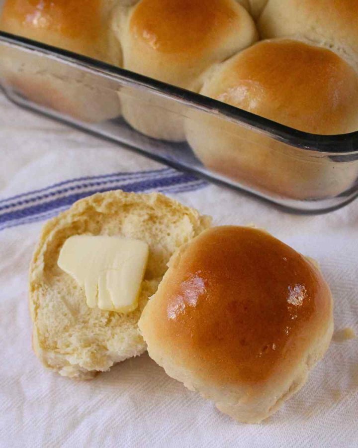 A close up of a buttered 1 hour dinner roll with the pan of dinner rolls in the background.