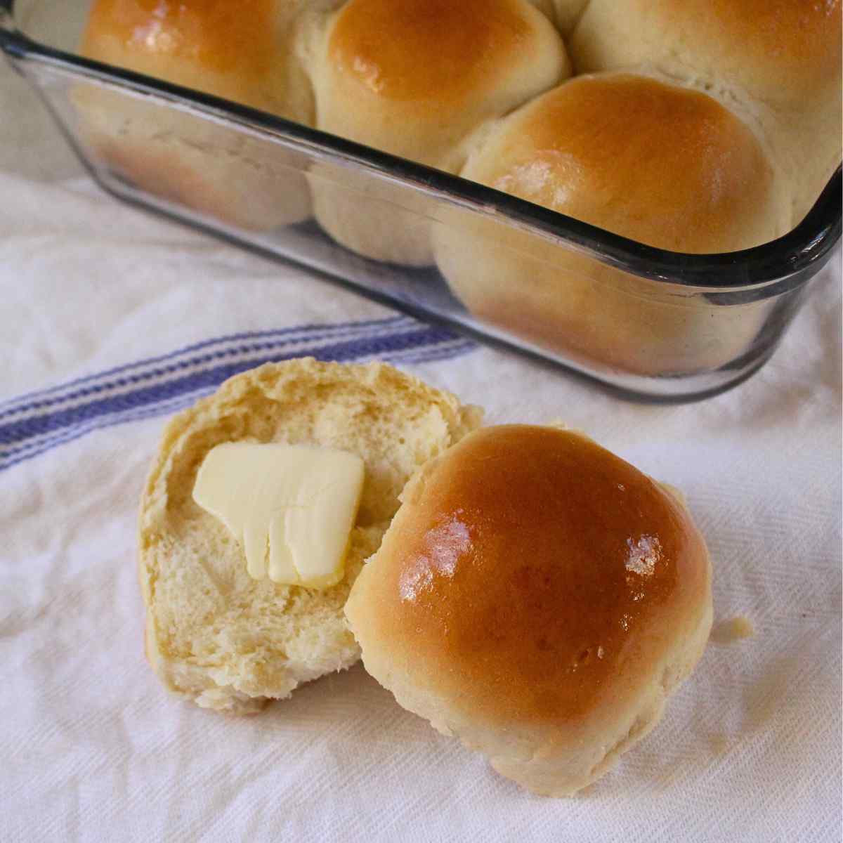 A close up of a buttered 1 hour dinner roll with the pan of dinner rolls in the background.