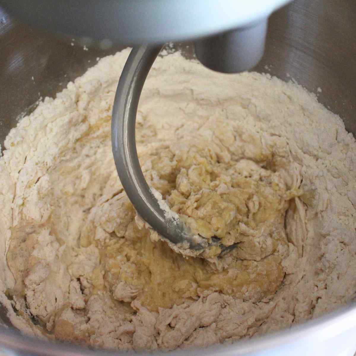 A dough hook mixing dinner roll ingredients together.