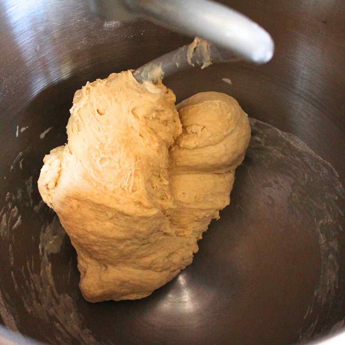 A dough hook with kneaded dough in a mixer bowl.