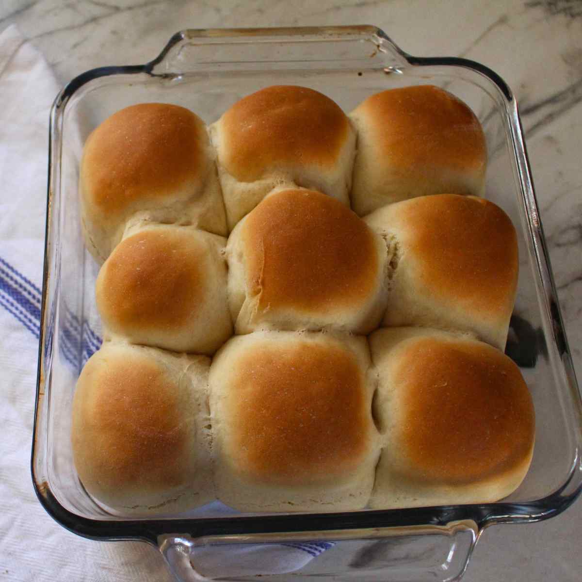 Baked and lightly brown dinner rolls in a glass baking pan.