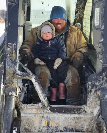 A man and small girl sitting in a skid steer.