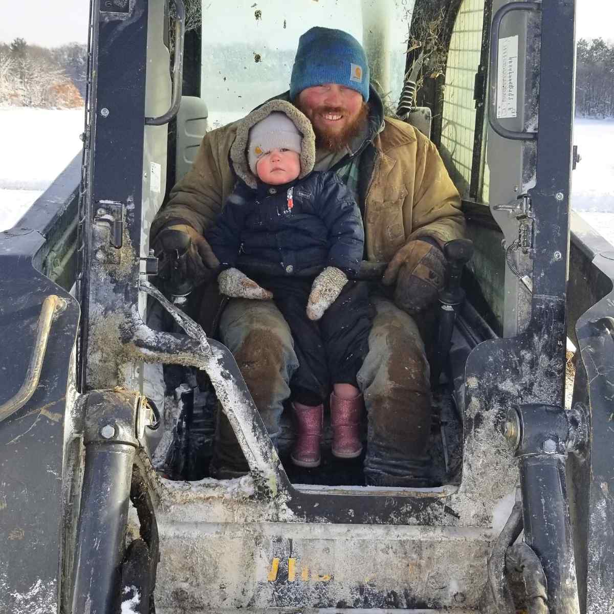 A man and small girl sitting in a skid steer.