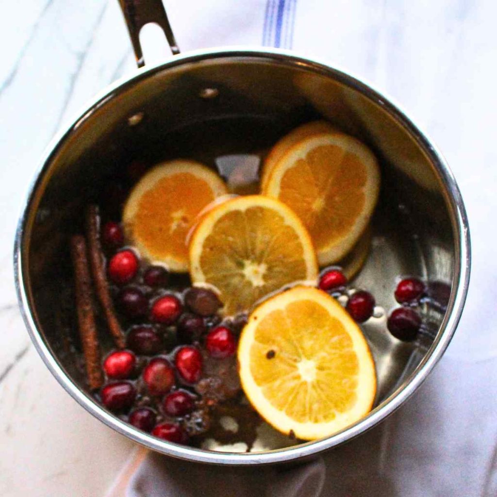 A pan filled with sliced oranges, cinnamon sticks, spices, cranberries and water for a Christmas simmer pot.