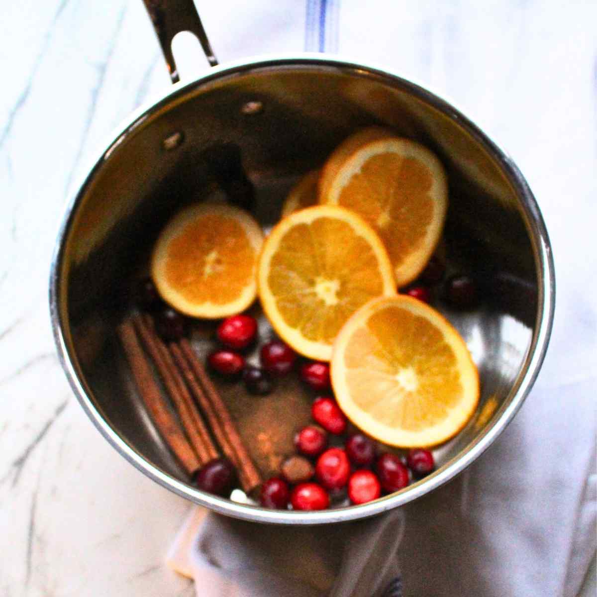 A pan filled with sliced oranges, cinnamon sticks, spices, and cranberries for a Christmas simmer pot.