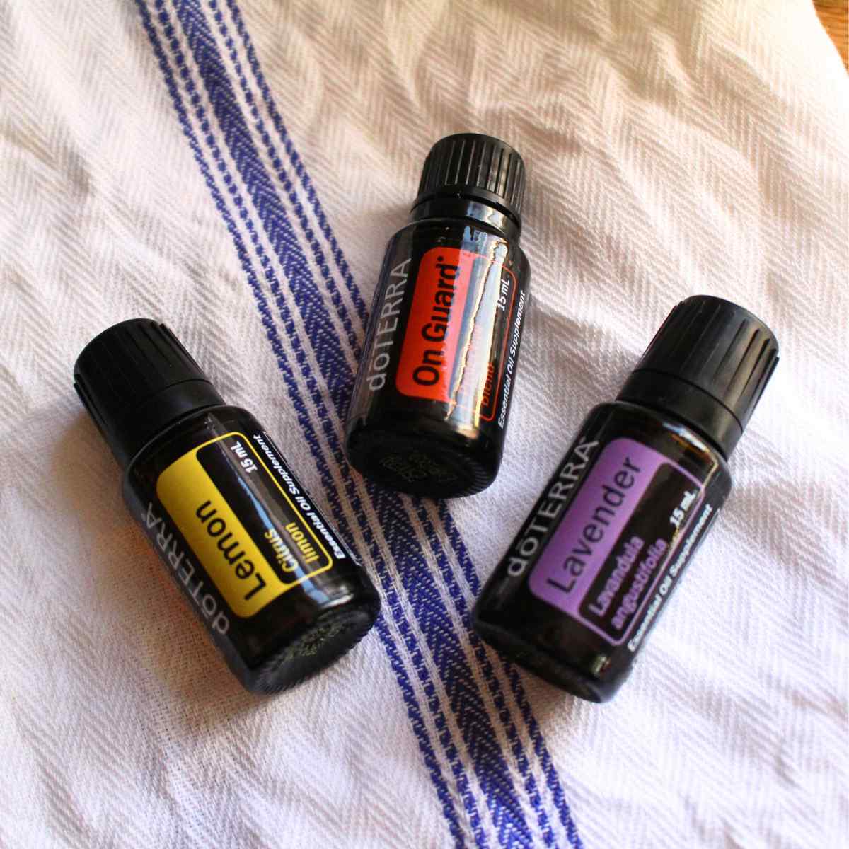 Three essential oil bottles of Lemon, On Guard, and Lavender on a tea towel.