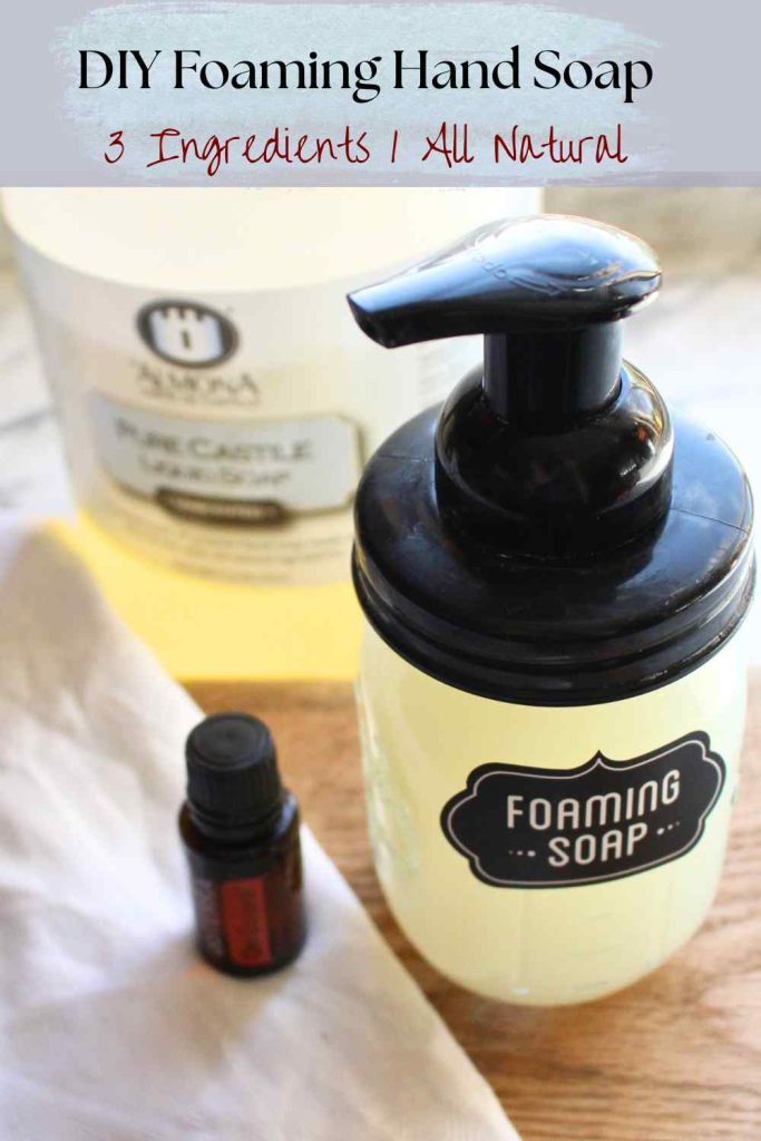 A filled bottle of DIY foaming hand soap with an essential oil bottle on the left and a jug of Castile soap in the background.