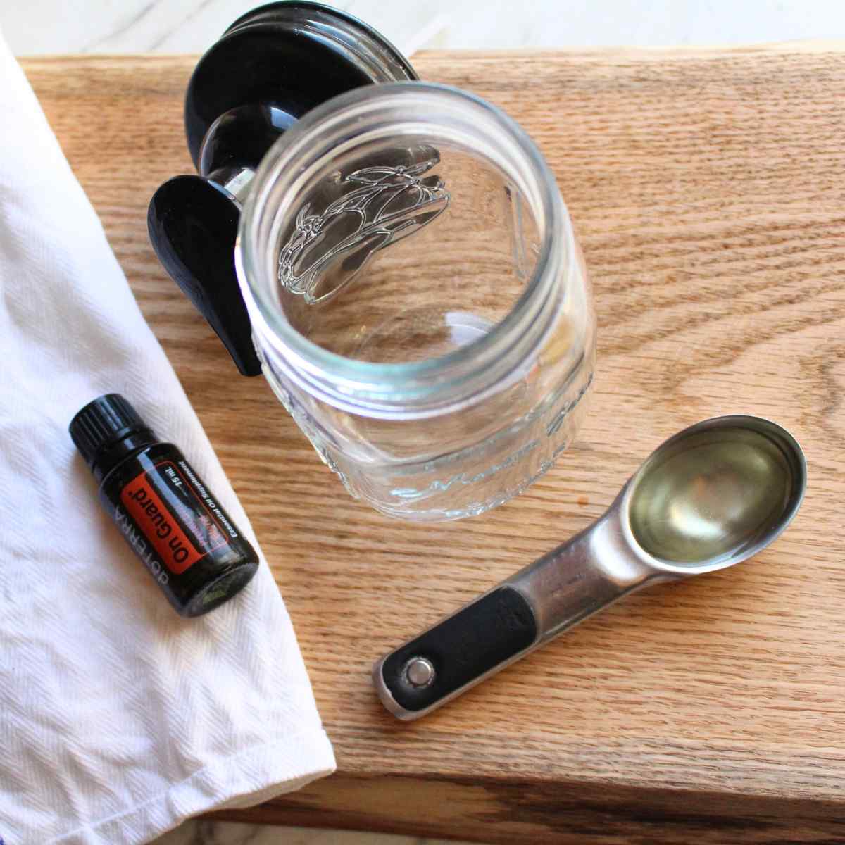 A close up view of an open foaming hand soap jar with an On Guard essential oil bottle on the left, and a tablespoon of Castile soap next to it on the right.