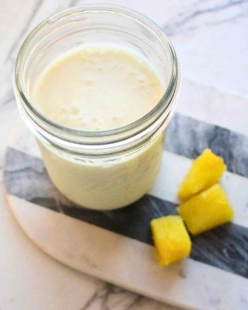 A mason jar of Pina colada kefir smoothie with pineapple pieces on the side.