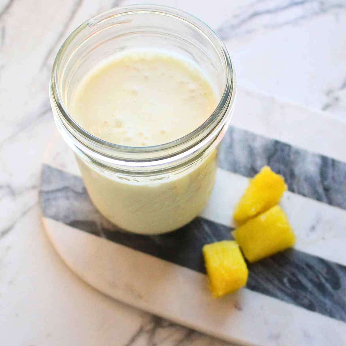 A mason jar of Pina colada kefir smoothie with pineapple pieces on the side.