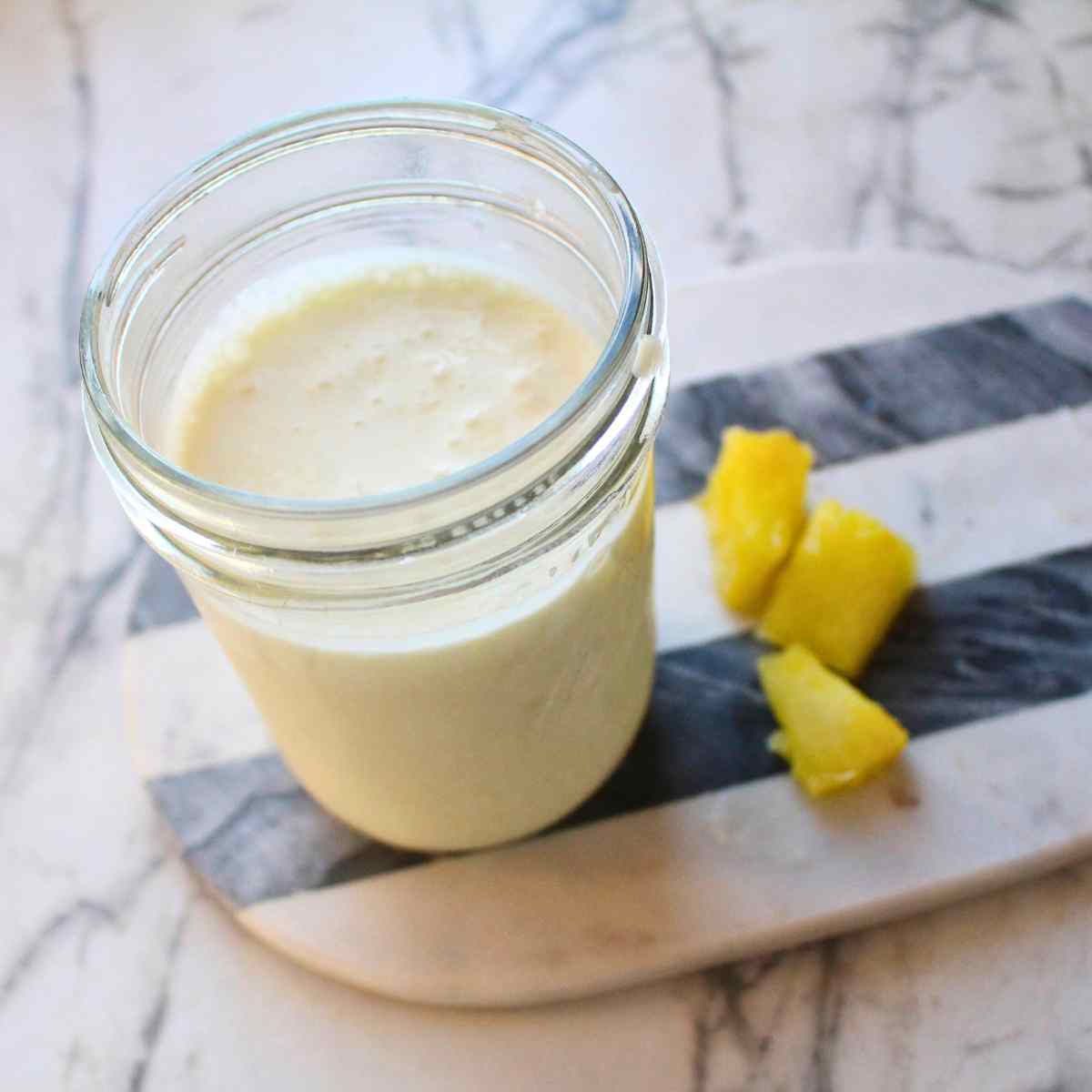 A mason jar of Pina colada kefir smoothie with pineapple pieces on the side.