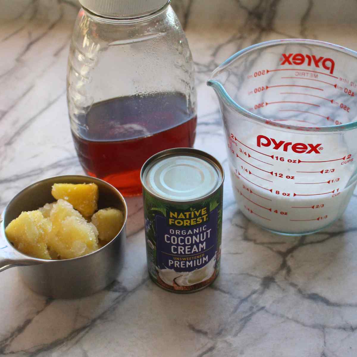 Ingredients including frozen pineapple in a measuring cup, a can of coconut cream, kefir in a measuring cup, and honey in a jar for Pina Colada Kefir Smoothies.