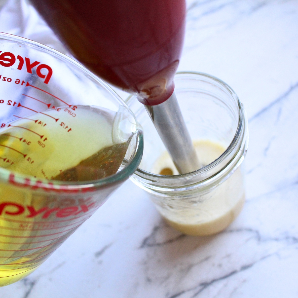 Avacado oil being poured into a glass jar with an immersion blender.