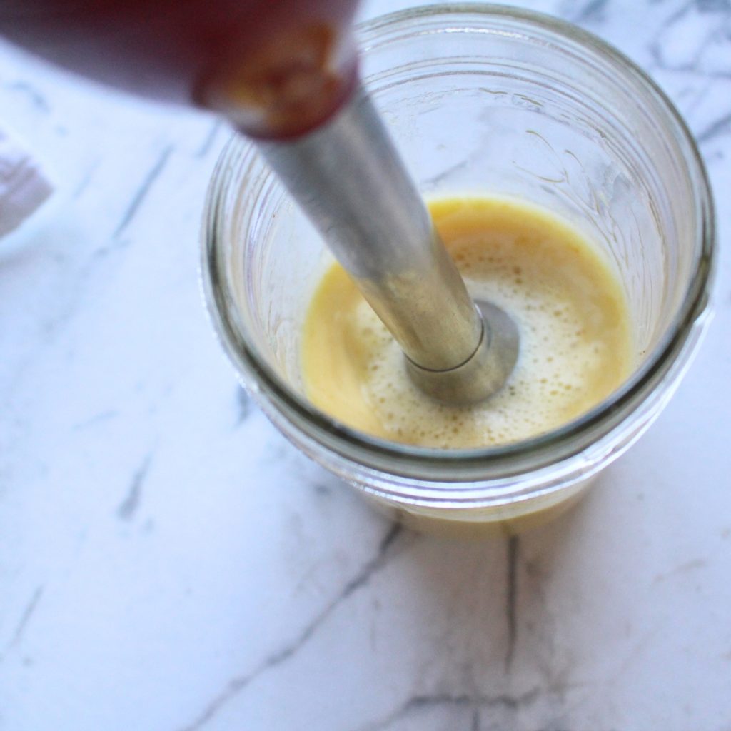 An immersion blender blending an egg mixture for homemade miracle whip.