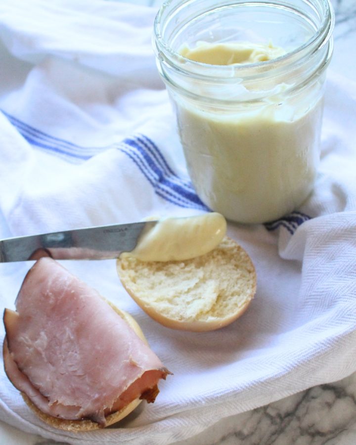 Homemade miracle whip being spread with a knife on sandwich bread.