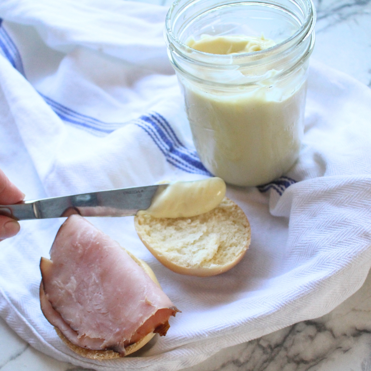 Homemade miracle whip being spread with a knife on sandwich bread.