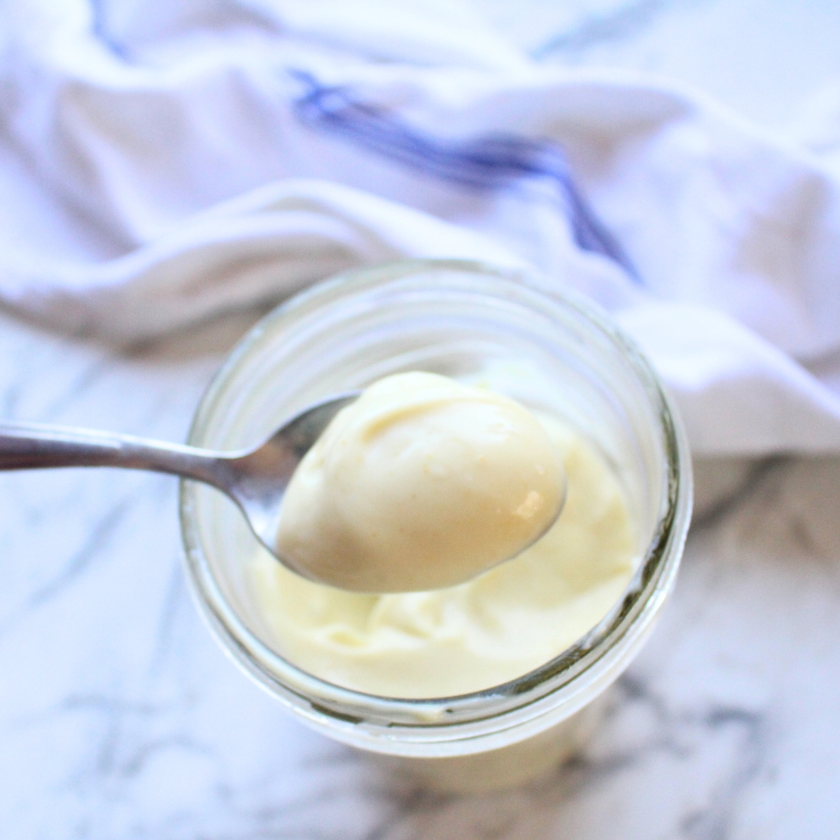 A spoon over a glass jar holding homemade miracle whip.